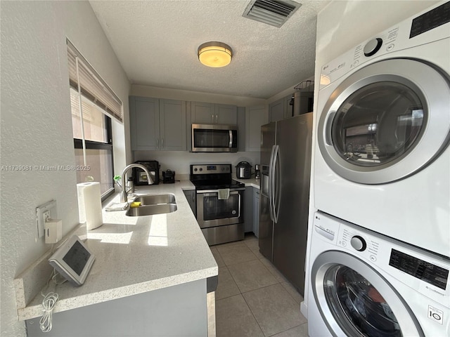 washroom featuring stacked washer / drying machine, light tile patterned floors, sink, and a textured ceiling