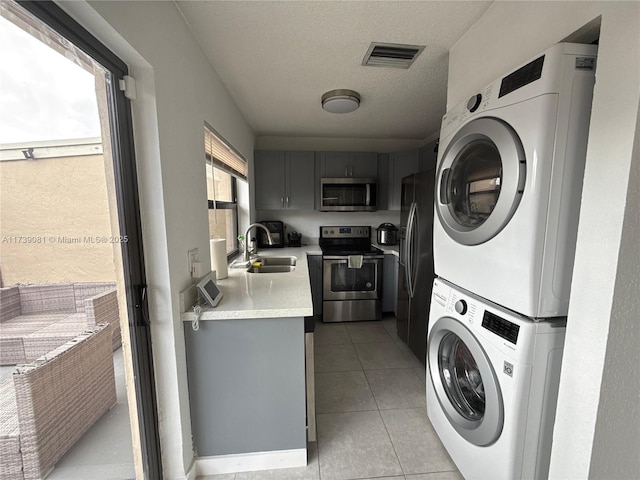 laundry area featuring stacked washer / dryer, sink, a textured ceiling, and light tile patterned floors