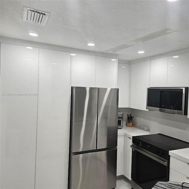 kitchen featuring a textured ceiling, stainless steel appliances, and white cabinets