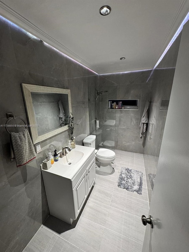 bathroom with a tile shower, tile walls, vanity, toilet, and tile patterned floors