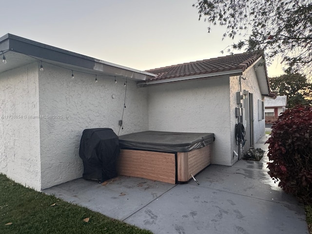 property exterior at dusk with a patio area and a hot tub