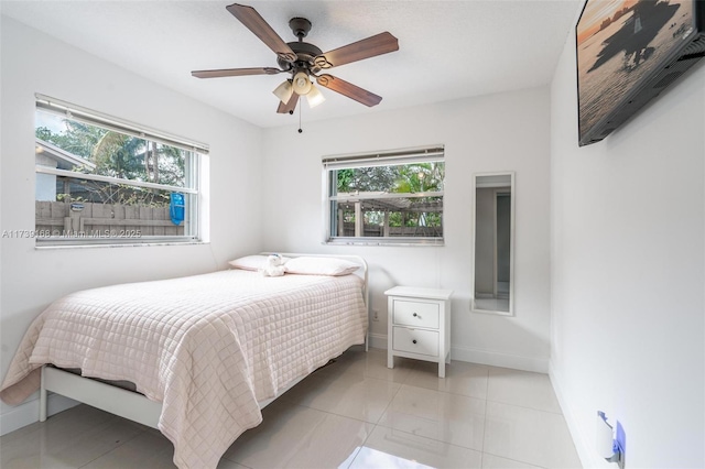 bedroom featuring light tile patterned floors, multiple windows, baseboards, and a ceiling fan
