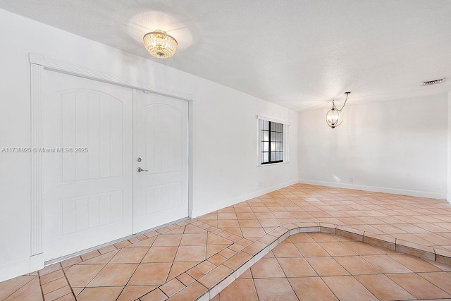 entryway featuring a chandelier, a textured ceiling, and light tile patterned floors