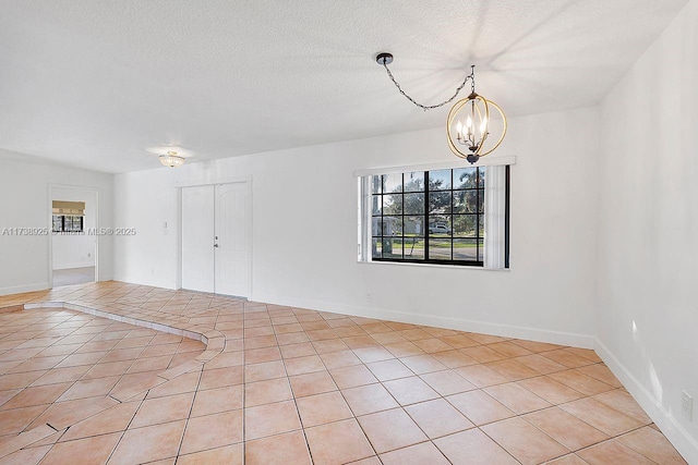 unfurnished room with an inviting chandelier, a textured ceiling, and light tile patterned floors