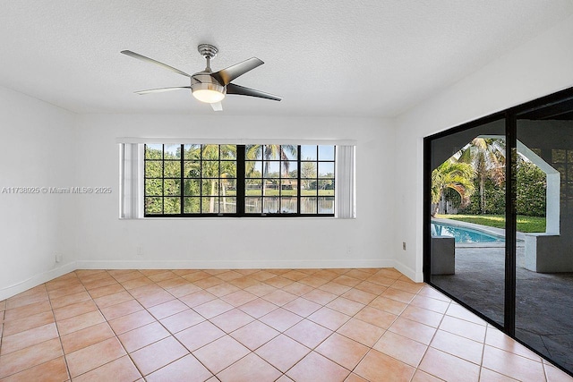 empty room with ceiling fan, a textured ceiling, and light tile patterned floors