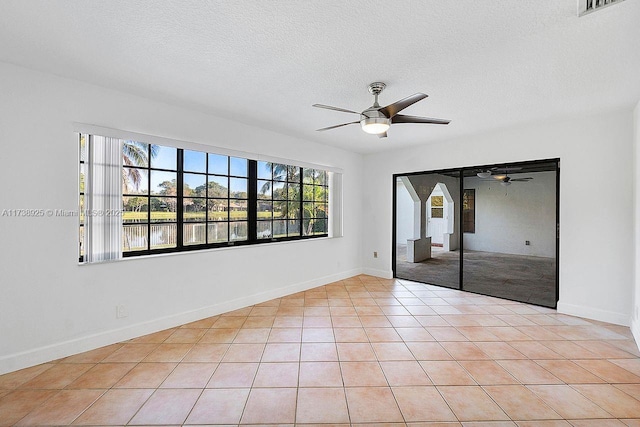 empty room featuring light tile patterned flooring, a water view, ceiling fan, and a textured ceiling