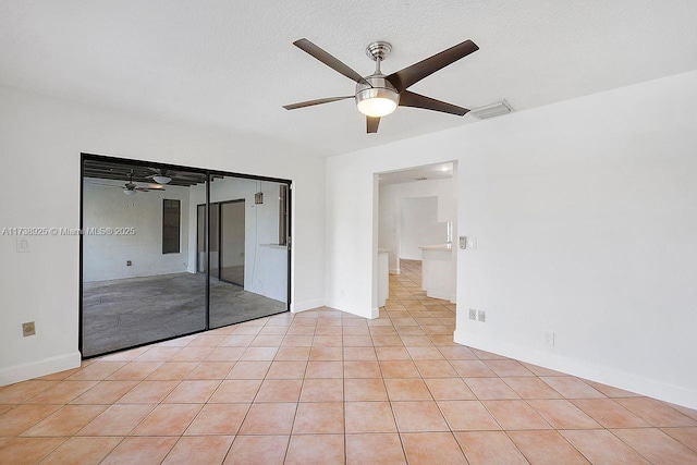 empty room featuring a textured ceiling, ceiling fan, and light tile patterned flooring