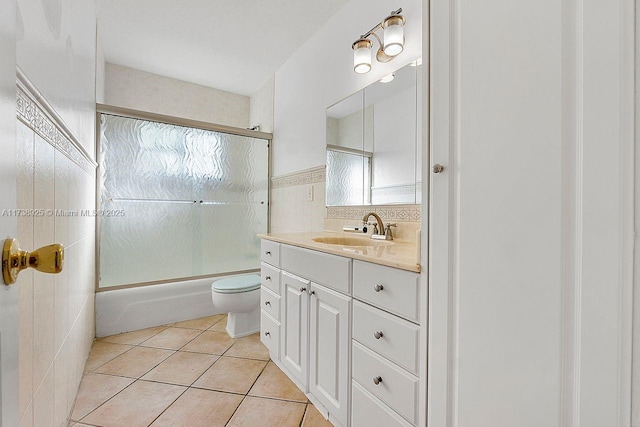 full bathroom featuring combined bath / shower with glass door, tile patterned flooring, tile walls, vanity, and toilet