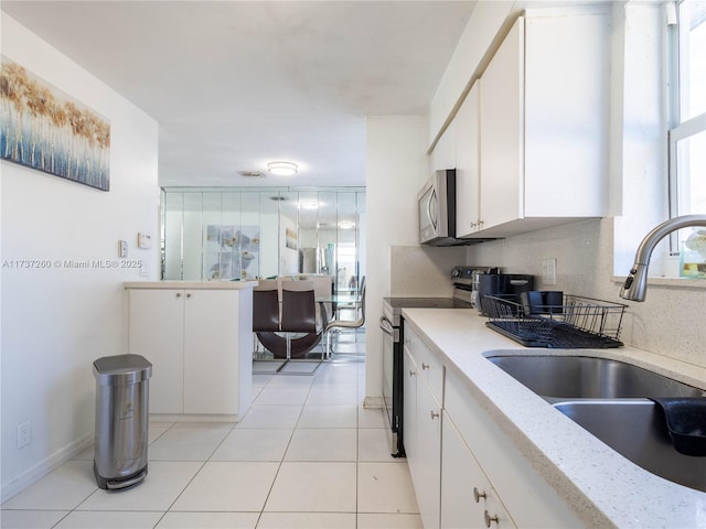 kitchen with sink, light tile patterned floors, appliances with stainless steel finishes, backsplash, and white cabinets