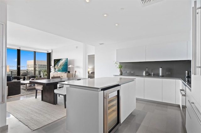 kitchen featuring white cabinets, a kitchen island, wine cooler, and backsplash