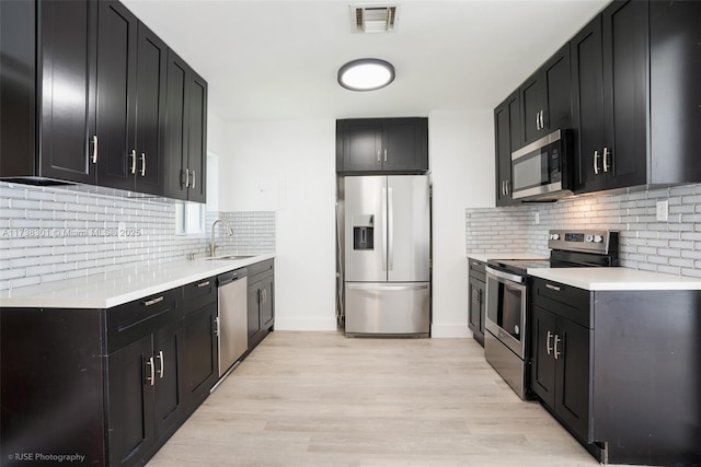 kitchen featuring visible vents, light wood-type flooring, a sink, appliances with stainless steel finishes, and dark cabinets