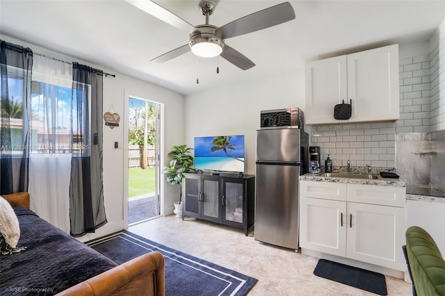 interior space with light stone counters, freestanding refrigerator, a sink, decorative backsplash, and white cabinets