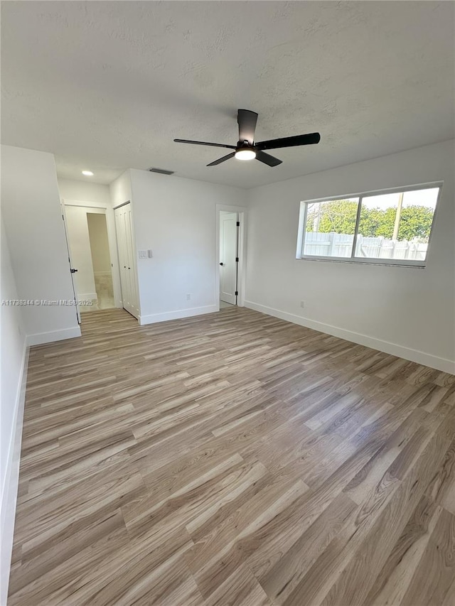 empty room with ceiling fan, a textured ceiling, and light wood-type flooring