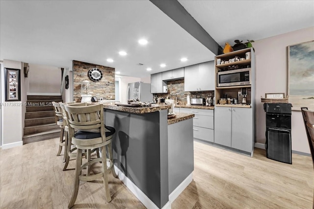 kitchen featuring appliances with stainless steel finishes, dark stone counters, light hardwood / wood-style flooring, and backsplash