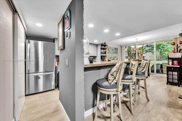 kitchen featuring stainless steel fridge, light stone countertops, light hardwood / wood-style floors, a kitchen bar, and kitchen peninsula