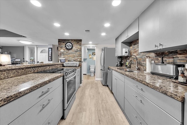 kitchen featuring gray cabinets, appliances with stainless steel finishes, tasteful backsplash, sink, and dark stone countertops