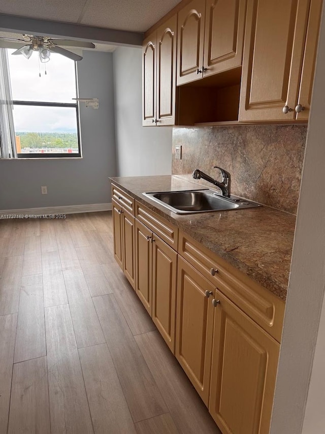 kitchen with sink, dark stone countertops, ceiling fan, light hardwood / wood-style floors, and decorative backsplash