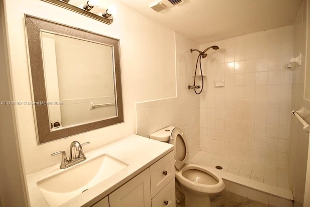 bathroom featuring a tile shower, vanity, and toilet