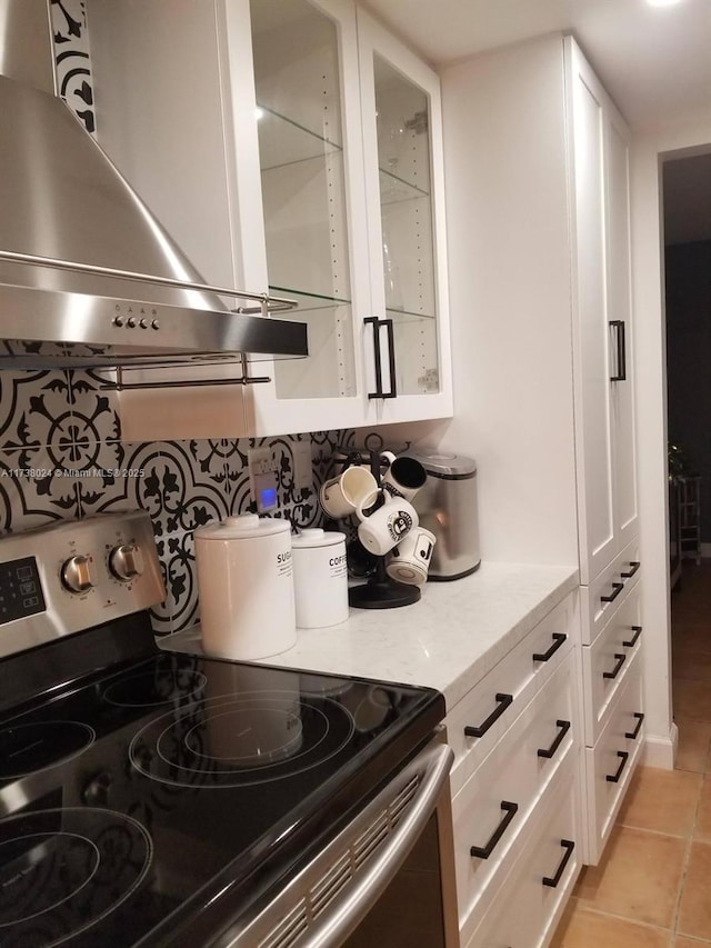 kitchen featuring electric stove, white cabinetry, island exhaust hood, light stone countertops, and light tile patterned flooring