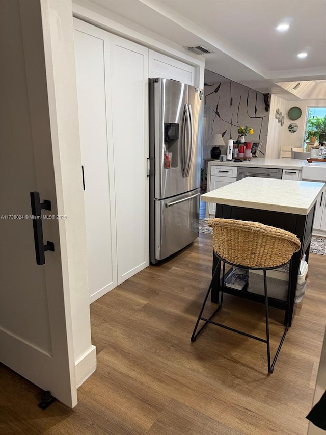 kitchen featuring white cabinetry, stainless steel appliances, a kitchen breakfast bar, a center island, and wood-type flooring