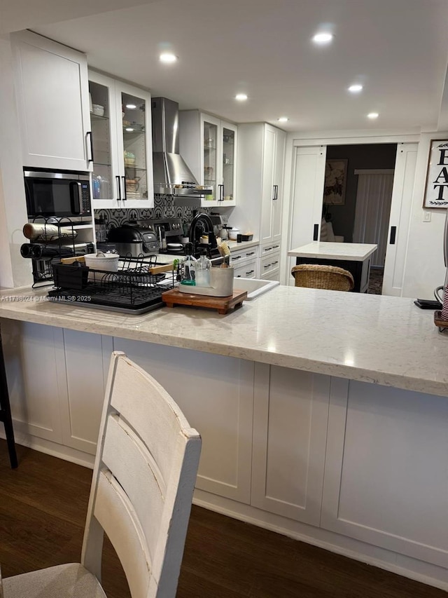 kitchen with light stone counters, wall chimney range hood, white cabinetry, and dark hardwood / wood-style floors