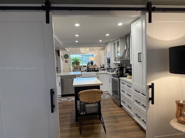 kitchen with white cabinets, appliances with stainless steel finishes, a barn door, and wall chimney range hood