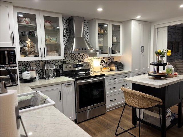 kitchen featuring stainless steel electric range, dark hardwood / wood-style floors, white cabinets, wall chimney range hood, and backsplash