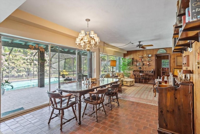 dining area with wooden walls and ceiling fan with notable chandelier