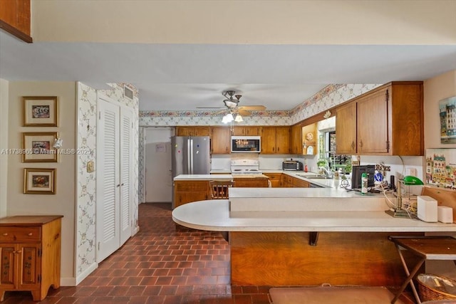 kitchen with a breakfast bar, sink, kitchen peninsula, ceiling fan, and white range