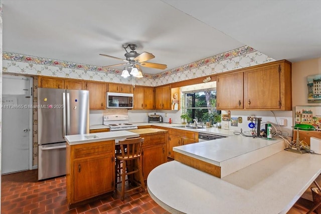 kitchen with sink, a breakfast bar, ceiling fan, stainless steel appliances, and kitchen peninsula