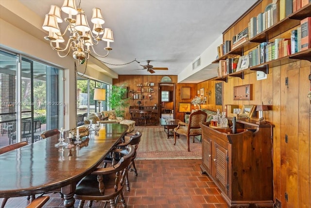 dining area with ceiling fan with notable chandelier and wood walls