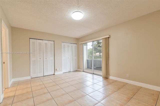 unfurnished bedroom with light tile patterned floors, two closets, a textured ceiling, access to outside, and baseboards