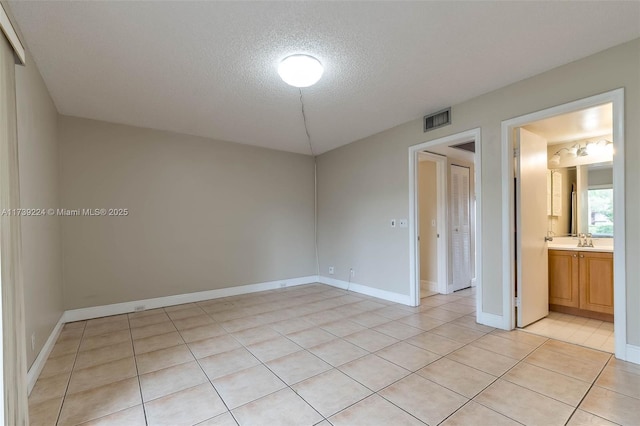 empty room featuring baseboards, visible vents, a textured ceiling, a sink, and light tile patterned flooring