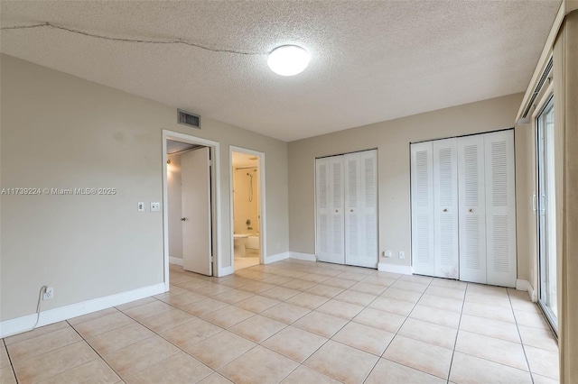 unfurnished bedroom featuring light tile patterned floors, baseboards, visible vents, a textured ceiling, and multiple closets