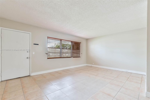 spare room featuring a textured ceiling, light tile patterned floors, and baseboards