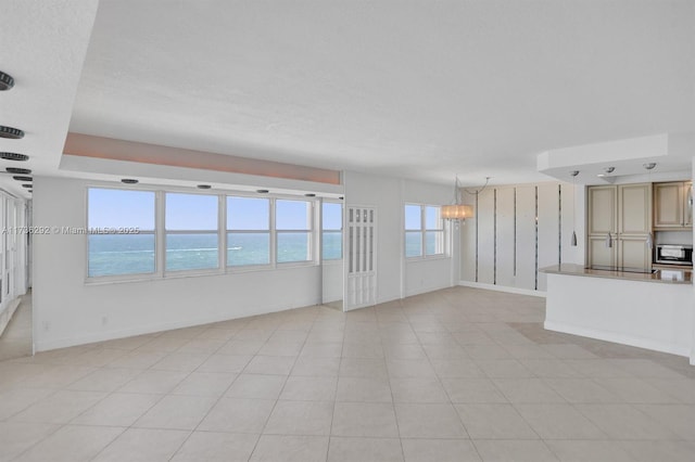 unfurnished living room featuring a water view, an inviting chandelier, a textured ceiling, and light tile patterned floors