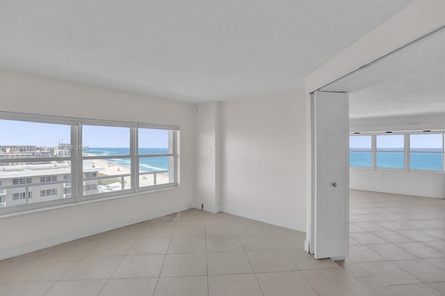 empty room with a view of the beach, light tile patterned floors, a textured ceiling, and a water view