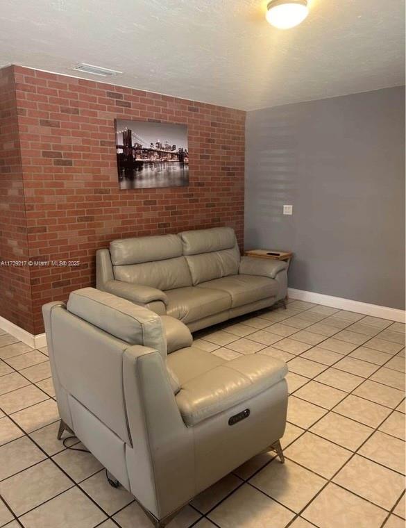 living room with brick wall, a textured ceiling, and light tile patterned floors