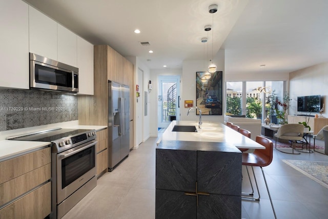 kitchen with sink, a kitchen island with sink, hanging light fixtures, white cabinetry, and stainless steel appliances