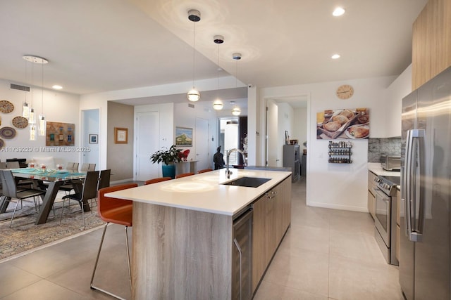 kitchen with sink, tasteful backsplash, an island with sink, pendant lighting, and stainless steel appliances