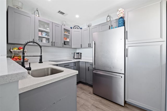 kitchen with sink, stainless steel fridge, gray cabinetry, light stone countertops, and light wood-type flooring