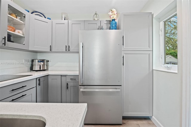 kitchen with light hardwood / wood-style flooring, stainless steel fridge, gray cabinets, black electric stovetop, and light stone countertops