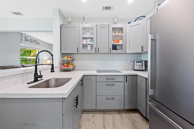 kitchen with sink, gray cabinetry, stainless steel fridge, black electric stovetop, and light hardwood / wood-style floors