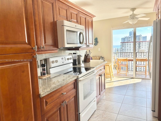 kitchen with backsplash, light tile patterned floors, ceiling fan, light stone counters, and white appliances