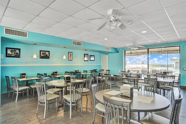 dining area with a drop ceiling, hardwood / wood-style flooring, and ceiling fan