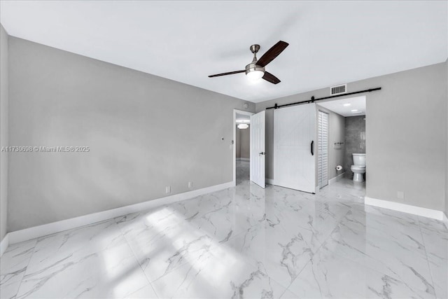 unfurnished bedroom featuring ceiling fan, ensuite bath, and a barn door