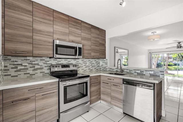 kitchen with sink, light tile patterned floors, appliances with stainless steel finishes, tasteful backsplash, and kitchen peninsula