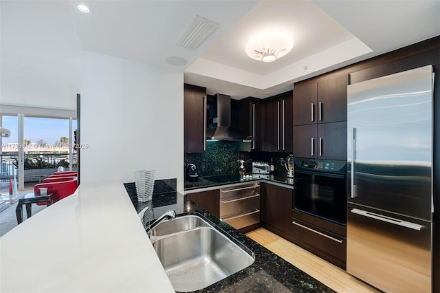 kitchen featuring sink, black appliances, light hardwood / wood-style floors, decorative backsplash, and wall chimney exhaust hood