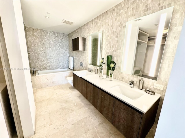 full bathroom with visible vents, a garden tub, a sink, tile walls, and double vanity