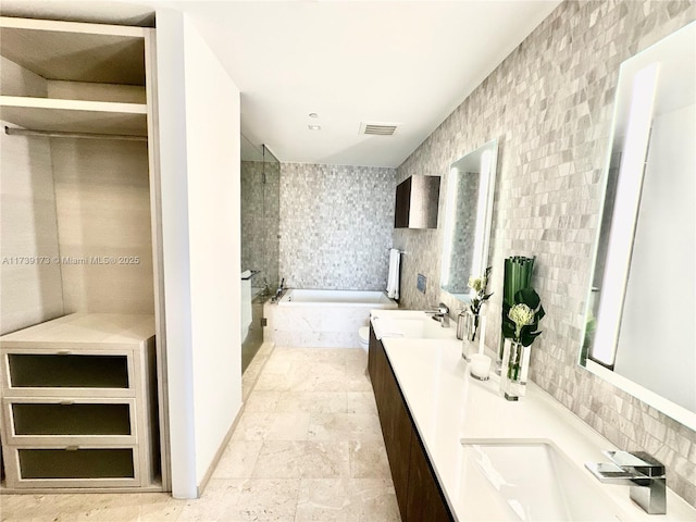 bathroom featuring visible vents, a garden tub, double vanity, tile walls, and a sink